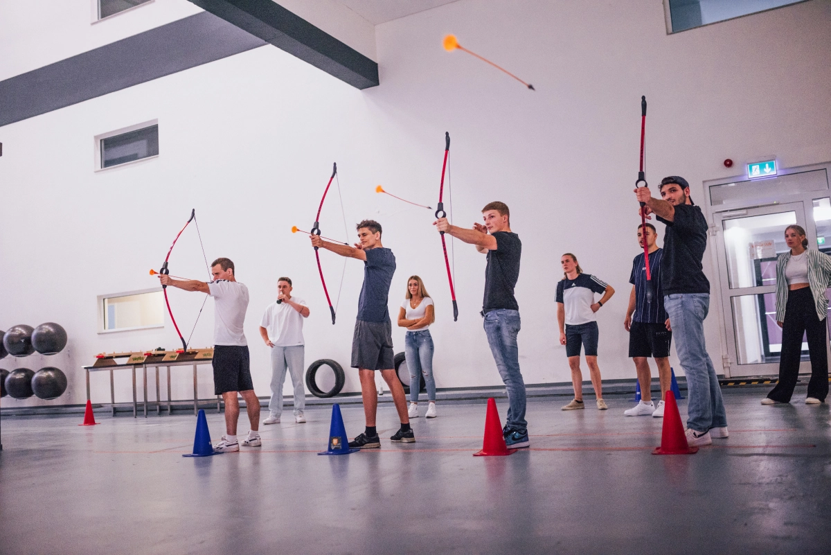 mehrere teilnehmer schiessen gleichzeitig mit pfeil und bogen auf zielscheiben – team action pur
